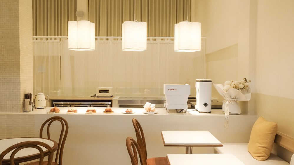 A stylish corner of the restaurant interior showcasing mid-century modern furniture, soft neutral-toned upholstery, and a minimalist gallery wall. The warm ambient lighting creates a sophisticated yet welcoming vibe.